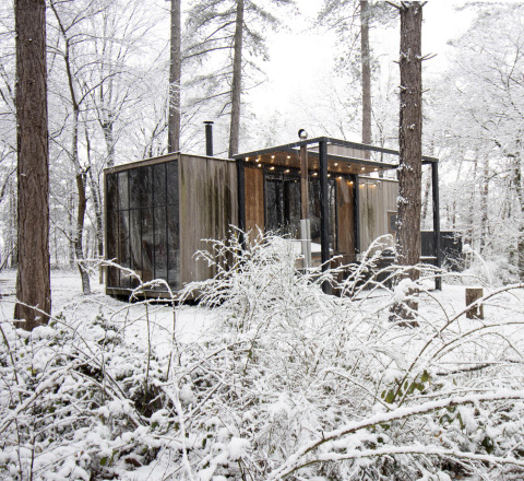 Cabane enneigée avec grandes baies vitrées et guirlande lumineuse en forêt de Limburg, Belgique.