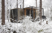 Cabaña cubierta de nieve con grandes ventanales y luces, situada en el bosque de Limburg, Bélgica.
