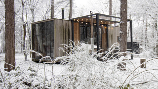 Sneeuwbedekte cabine met grote ramen en sfeerverlichting in het bos van Limburg, België.