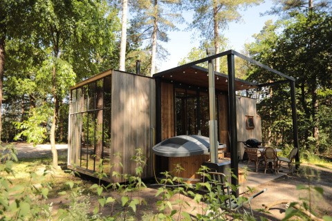 Moderne houten cabin in het bos met grote ramen, hottub en gezellig terras met zitje buiten.