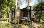 Moderne Holzhütte im Wald mit großen Fenstern, Terrasse, Whirlpool und gemütlicher Sitzecke.