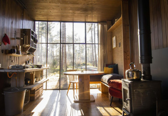 Interno di una cabina accogliente con grandi finestre, stufa a legna e vista boschiva a Limburg, Belgio.