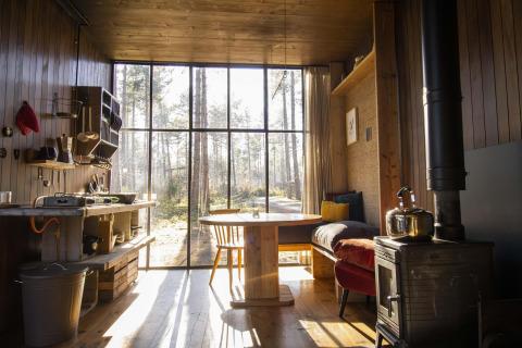 Intérieur d'une cabane en bois avec grandes fenêtres, poêle et vue sur la forêt à Limburg, Belgique.