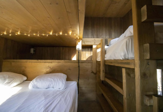 Knusse glampingruimte met houten stapelbedden, sfeerverlichting en gelambriseerde houten wanden.