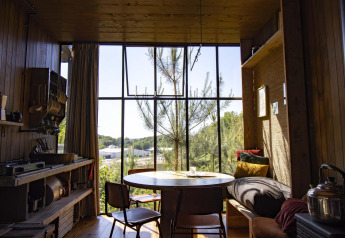 Interno di accogliente cabina in legno con ampia finestra, tavolo e vista sulla foresta a Limburgo, Belgio.