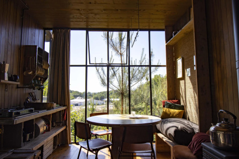 Gemütliche Holzhütte mit großem Fenster, Esstisch und Blick auf den Wald in Limburg, Belgien.