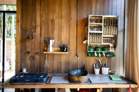 Cocina rústica de madera con fregadero de piedra y vajilla en cabaña de Cosy Cabins, bosque Limburg.