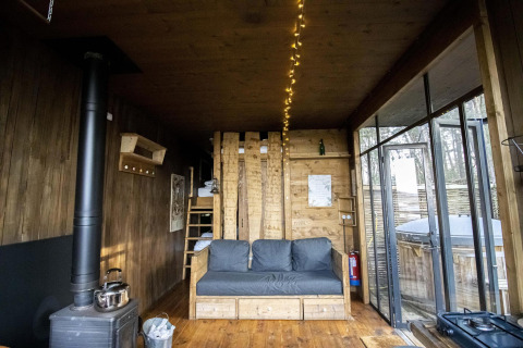 Innenansicht der Water Cabin mit Holzinterieur, Sofa, Kamin und großen Fenstern in Limburg, Belgien.