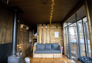 Interno della Water Cabin con pareti in legno, divano, stufa e grandi finestre a Limburg, Belgio.