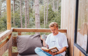 Homme lisant un livre et buvant un café sur un balcon d’une cabane dans les arbres en forêt de Limbourg, Belgique.