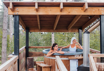 Twee vrouwen ontspannen in een buiten bubbelbad op een boomhut terras in het bos van Limburg, België.