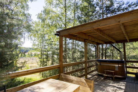 Terraza de madera cubierta con mesa y jacuzzi en la cabaña Comfort Sweet, Cosy Cabins, bosque de Limburg, Bélgica.