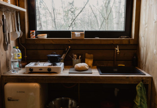 Rustic wooden cabin kitchen with stove, bread, and forest view at Comfort Sweet + hot tub in Limburg, Belgium.