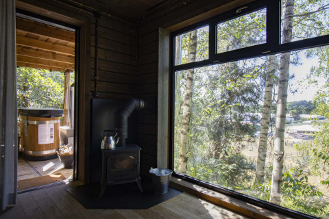 Vista desde la cabaña Comfort Sweet con estufa, gran ventanal y bañera exterior en el bosque de Limburgo.