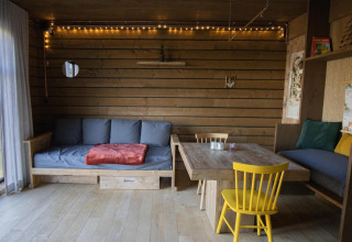 Gemütliche Kabine mit Holzverkleidung, Sofas, Esstisch und Lichterketten im Wald von Limburg, Belgien.