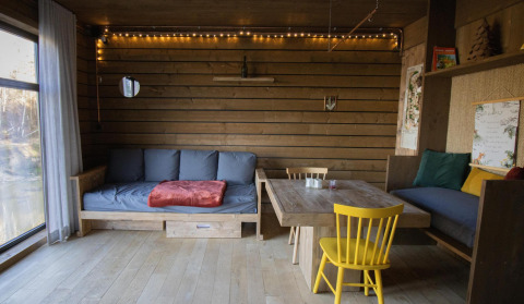 Gemütliche Kabine mit Holzverkleidung, Sofas, Esstisch und Lichterketten im Wald von Limburg, Belgien.