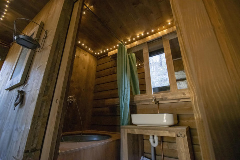 Baño rústico de cabaña con madera, cortina verde, bañera y luces cálidas en Limburg, Bélgica.