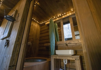 Gezellige houten badkamer met bad, gordijn en sfeerverlichting in een cabin in Limburg, België.