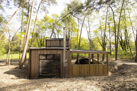 Cabaña Comfort Classic con bañera de hidromasaje, ubicada en medio del bosque y rodeada de árboles altos.