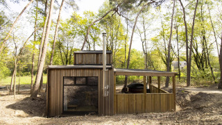 Cabaña Comfort Classic con bañera de hidromasaje, ubicada en medio del bosque y rodeada de árboles altos.