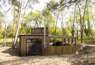 Comfort Classic blokhut met houten gevel en hot tub, te midden van hoge bomen in een bosrijke omgeving.