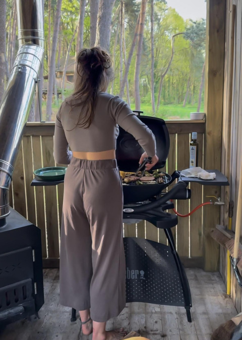 Mujer cocinando a la parrilla en la cabaña Comfort Classic + hot tub de Cosy Cabins, Limburg, Bélgica.