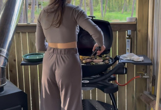 Mujer cocinando a la parrilla en la cabaña Comfort Classic + hot tub de Cosy Cabins, Limburg, Bélgica.