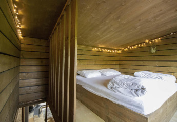 Letto soppalcato con lenzuola bianche, luci decorative e pareti in legno in una cabina con vasca idromassaggio in Limburgo, Belgio.