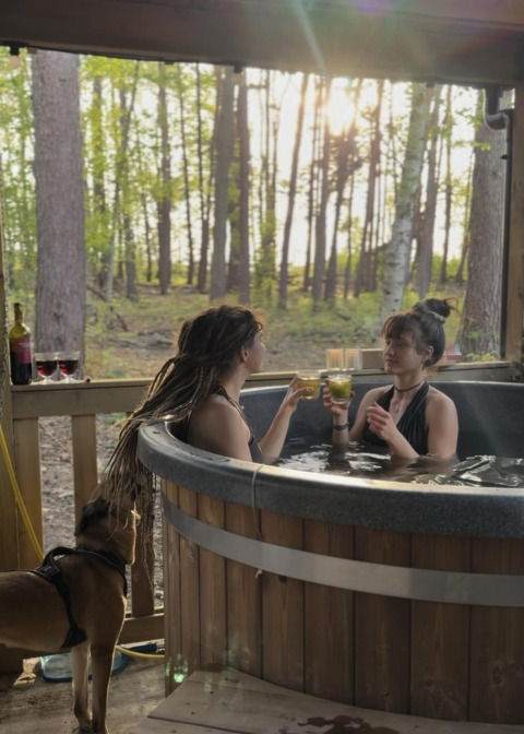 Dos mujeres disfrutan bebidas en la bañera de hidromasaje en Comfort Classic, Cosy Cabins, Limburg, Bélgica.