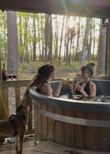 Dos mujeres disfrutan bebidas en la bañera de hidromasaje en Comfort Classic, Cosy Cabins, Limburg, Bélgica.
