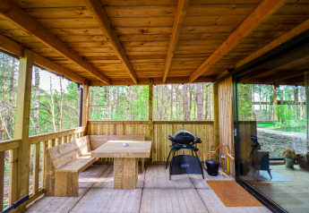 Terrazza coperta in legno con panca, tavolo e barbecue nel Comfort Classic + sauna cottage nella foresta di Limburg, Belgio.