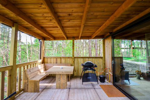 Terrasse en bois couverte avec banc, table et barbecue au Comfort Classic + sauna, forêt du Limbourg, Belgique.