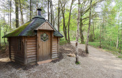 Cabaña Comfort Classic + sauna en Cosy Cabins, bosque de Limburg, Bélgica, rodeada de árboles verdes.
