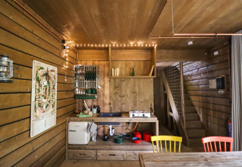 Interno cucina della cabina Comfort Classic + sauna, legno e sedie colorate nei boschi di Limburg, Belgio.