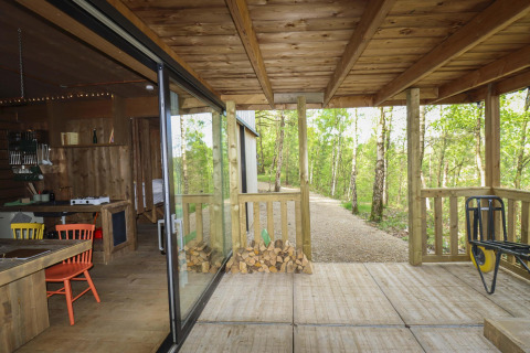 Cabaña de madera con terraza cubierta, vista al bosque y área de comedor interior, Cosy Cabins, Limburg.