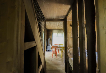 Interior de madera de la cabaña Comfort Classic + sauna en Cosy Cabins, bosque de Limburgo, Bélgica, con sillas de colores.
