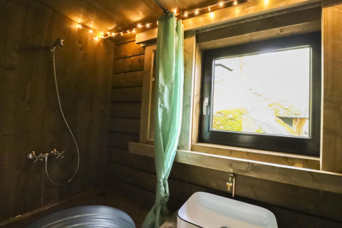Bagno rustico in cabina di legno con doccia, tenda verde e finestra affacciata sul bosco di Limburg.