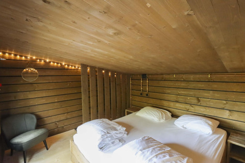 Dormitorio en Comfort Classic + sauna cottage en Cosy Cabins en el bosque de Limburg, Bélgica, con luces suaves.