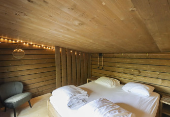 Camera da letto nel Comfort Classic + sauna cottage presso Cosy Cabins nella foresta di Limburgo, Belgio, con luci soffuse.