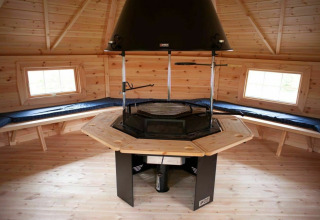 Interieur van houten lodge met centrale grill en banken bij Veluwe Villa + sauna, Holiday park De Boshoek, Nederland.