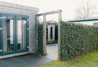 Buitenruimte van Veluwe Villa + sauna in vakantiepark De Boshoek, met haag en houten gebouwen.