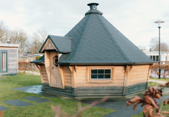 Kleine houten lodge met zwart dak bij vakantiepark De Boshoek in Nederland, omringd door gras.
