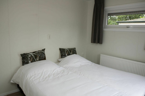 Modern bed with white bedding and nature-themed pillows in Veluwe Villa + sauna at De Boshoek Holiday Park, Netherlands.