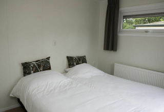 Moderne slaapkamer met wit beddengoed en natuurkussens in Veluwe Villa + sauna, Holiday park De Boshoek, Nederland.