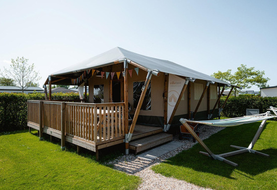 Villatent Cottage lodge met houten veranda en hangmat bij Camping de Molenhoek in Nederland, buitenaanzicht.