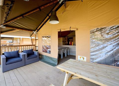 Zona exterior de descanso en una tienda safari de lujo, con sillones y una mesa de madera en la terraza.