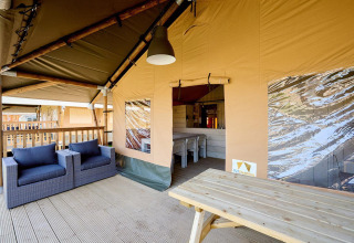 Zona exterior de descanso en una tienda safari de lujo, con sillones y una mesa de madera en la terraza.