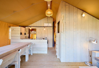 Indvendigt billede af en Villatent Cottage safari-telt med lyse trævægge, spisebord og køkken.