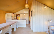 Binnenzicht van een Villatent Cottage safaritent met lichte houten wanden, tafel en keukenhoek.