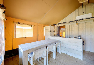 Vista interior de una tienda safari con mesa de madera, sillas y una pequeña cocina al fondo.